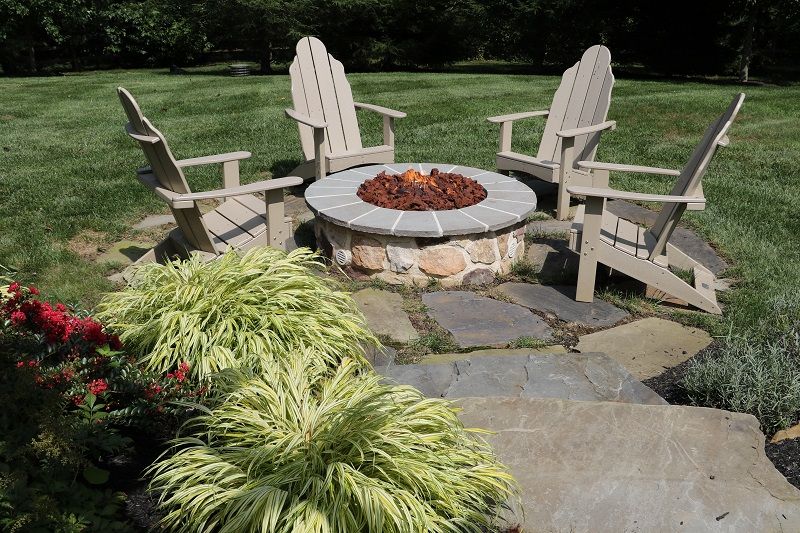 Circular fire pit with adirondack chairs surrounding on a stone patio | Outdoor Fireplaces and Firepits by Burkholder Landscape
