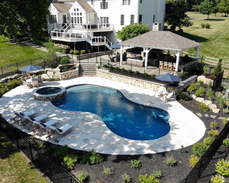 Backyard of a large white house with double layer deck, walkway to pavilion and pool with spa - Burkholder Landscape