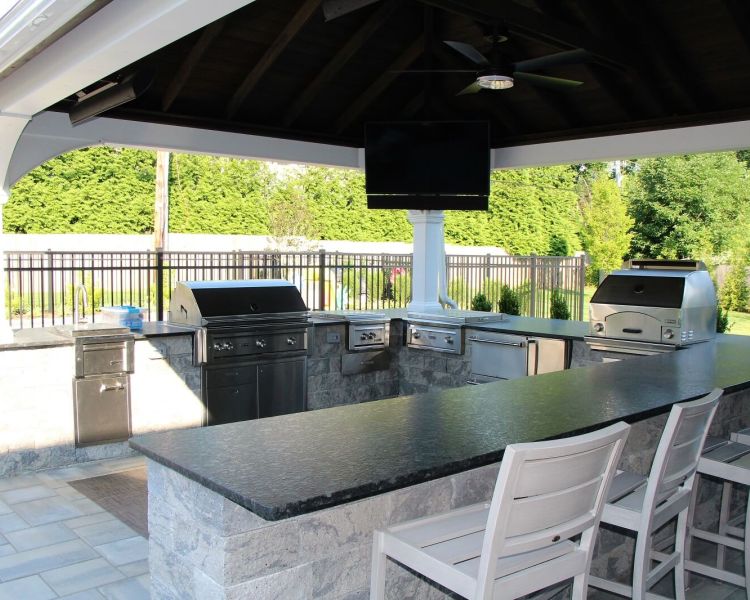 Outdoor kitchen under white pavilion, television and black countertops - Burkholder Landscape