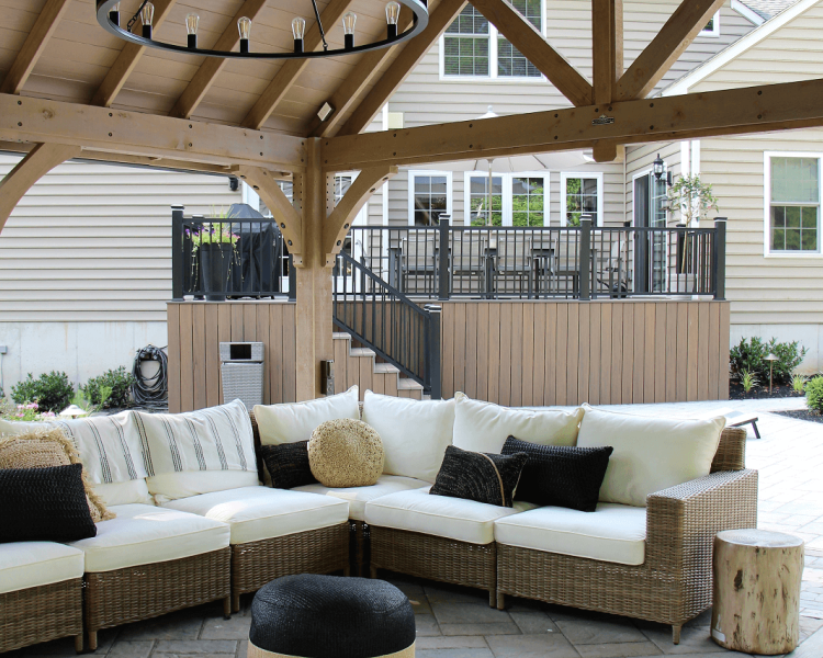 Pavilion with TV and seating area with white cushions and deck in the background -Burkholder Landscape