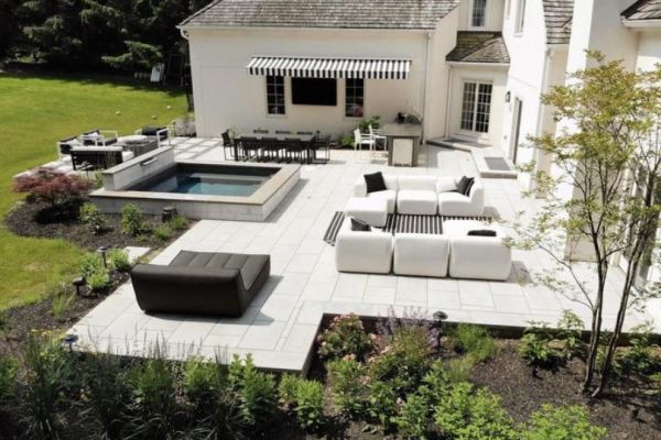 Backyard Oasis from side, outdoor furniture with black accessories, spa, outdoor kitchen and large Blu Grande pavers by Techo-Bloc - by Burkholder Landscape