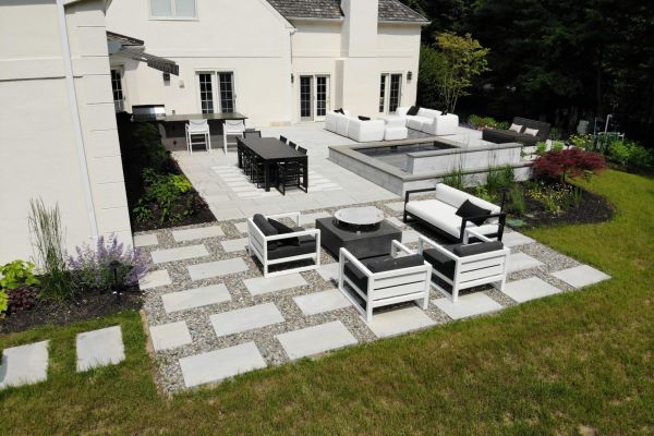Backyard Oasis from rear, outdoor furniture with black accessories, spa, outdoor kitchen and large Blu Grande pavers by Techo-Bloc - by Burkholder Landscape