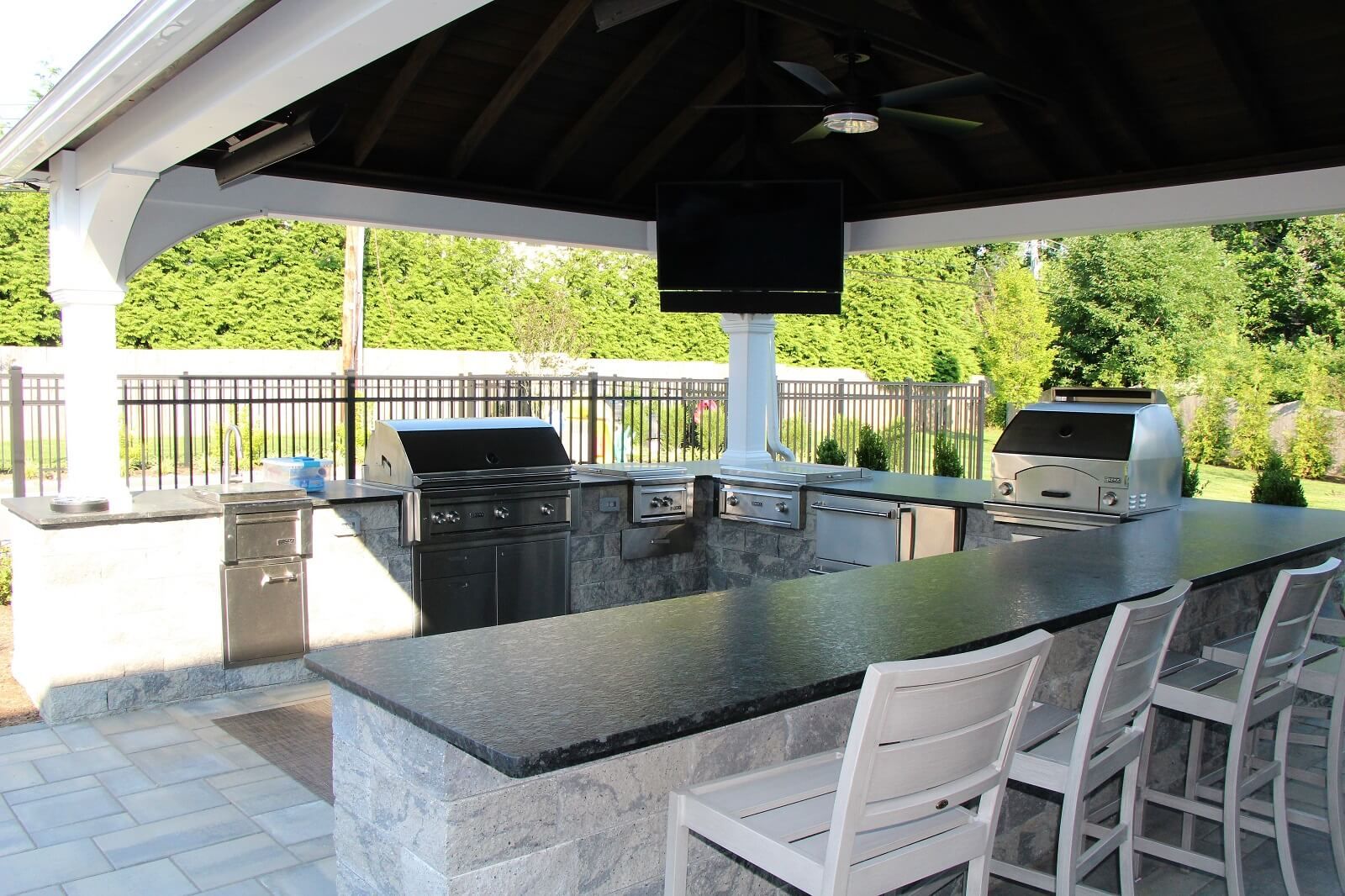 Outdoor kitchen under white pavilion, television and black countertops - Investing in Landscape Design - Burkholder Landscape