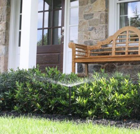 front porch of a home with a bench  and shrubs with a sprinkler running | lwn during drought | Burkholder Landscape