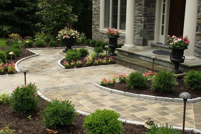 Front stone walk with manicured plant beds and columned entrance | Burkholder Landscape