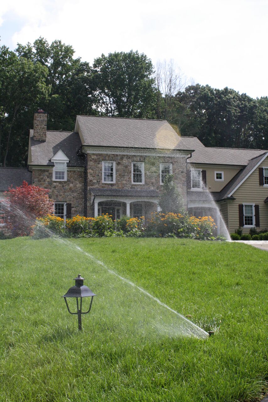 sprinklers running on a lawn with yard lights and a house in background | how to care for a lawn during drought Burkholder Landscape and Sir Sprinkler