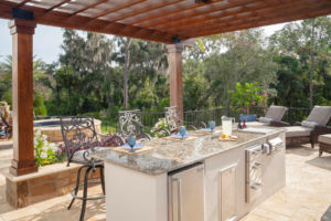 Pergola over outdoor kitchen with chaise lounges and a spa in the background