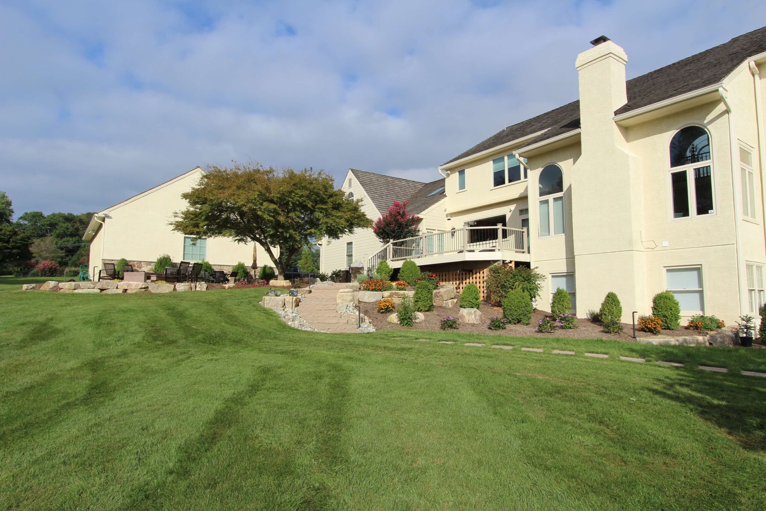 green lawn with plant beds near pale yellow house | Custom lawn care program | Burkholder Landscape