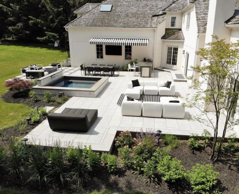 Backyard Oasis from side, outdoor furniture with black accessories, spa, outdoor kitchen and large Blu Grande pavers by Techo-Bloc - by Burkholder Landscape