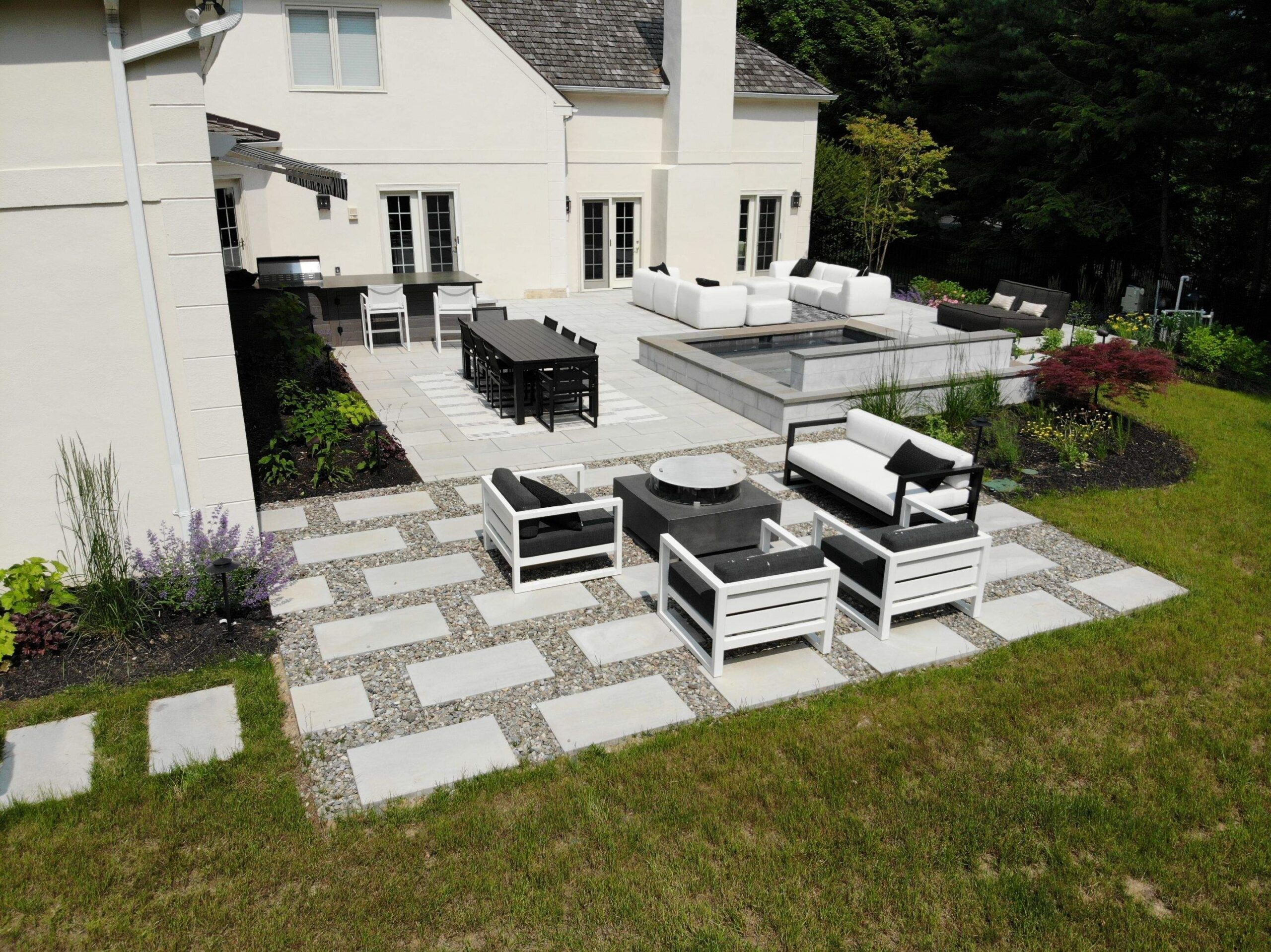 Backyard Oasis from rear, outdoor furniture with black accessories, spa, outdoor kitchen and large Blu Grande pavers by Techo-Bloc - by Burkholder Landscape