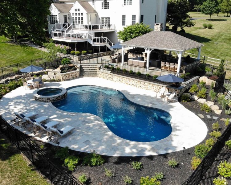 Backyard of a large white house with double layer deck, walkway to pavilion and pool with spa - Burkholder Landscape