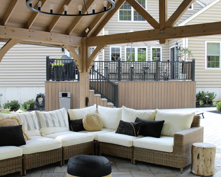Pavilion with TV and seating area with white cushions and deck in the background -Burkholder Landscape