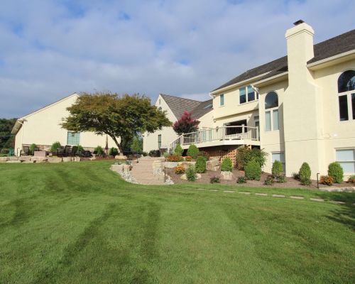 green lawn with plant beds near pale yellow house | Custom lawn care program | Burkholder Landscape